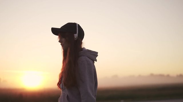 silhouette of a girl in headphones against the setting sun in nature. slow motion.