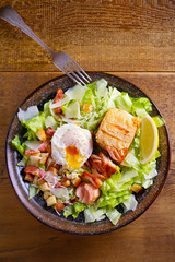 Salmon caesar salad. Crispy pan fried salmon fillet, bacon, poached egg, romaine lettuce and croutons in bowl on wooden table. overhead, vertical
