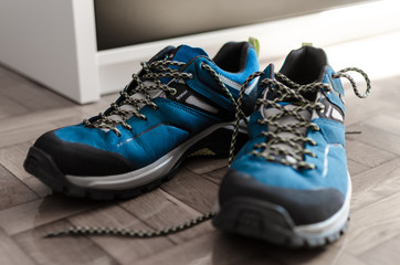 Par de zapatillas nuevas de monta&ntilde;a de color azul sobre un suelo de madera. Listas para salir a recorrer el la monta&ntilde;a y tener grandes aventuras