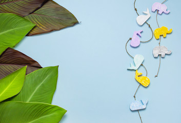 Tropical palm leaves and multi-colored childrens wooden toys in the form of elephants, whales on blue background top view with copy space. Minimal nature summer concept. Flat lay.