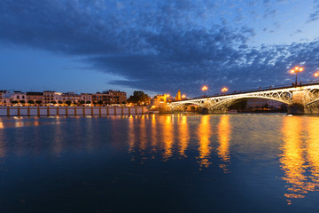 Obraz premium Seville in Spain. Waterfront night view of the old town and historical bridge