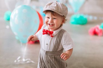 Happy baby boy celebrating first birthday. Kids birthday party decorated with balloons and colorful banner