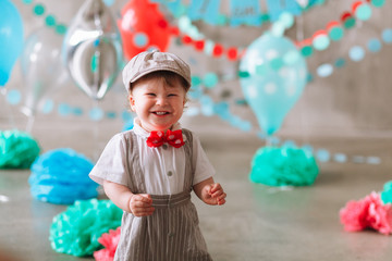 Happy baby boy celebrating first birthday. Kids birthday party decorated with balloons and colorful banner