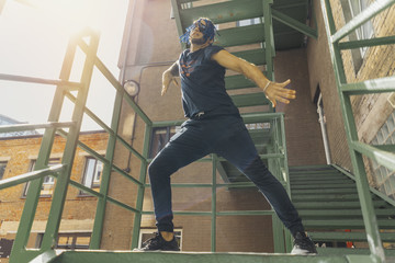 Young man with blue dreadlocks dancing reggaeton on green stairs.