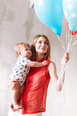 Mother and little boy celebrating first birthday. Woman holding balloons on concrete wall background