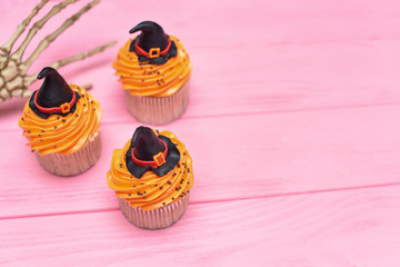 Halloween cupcakes. Witch's hat cupcake. Halloween treats on wooden pink background with palm of the skeleton.