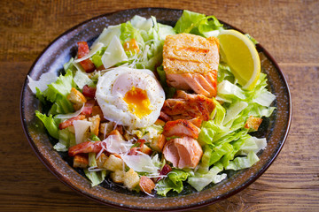Salmon caesar salad. Crispy pan fried salmon fillet, bacon, poached egg, romaine lettuce and croutons in bowl on wooden table. horizontal