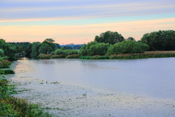 Beautiful view on town from river side on sunset. Green trees and plants on blue sky background. Nice nature landscape backgrounds.