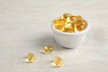 Bowl with cod liver oil pills on light background