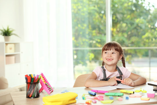 Cute girl doing homework at table with school stationery indoors