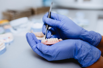 Dental prosthesis, prosthetics work. Close up of prosthetic's hands while working on the denture. Selective focus.
