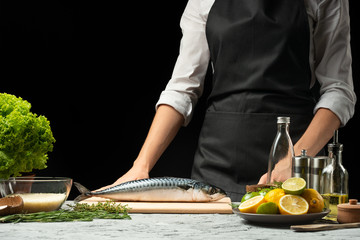 Preparation of mackerel by the chef, on a black background with lemons, limes
