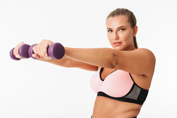Fototapeta na wymiar Pretty plump girl in sporty top doing exercises with dumbbells while dreamily looking in camera over white background. Plus size model