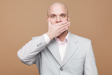 Pointing finger and amazed portrait of handsome middle aged businessman in classic light gray suit standing, looking at camera, wondering and showing brown background. indoor studio shot, isolated.