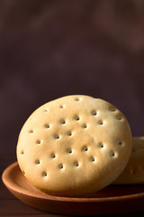 Traditional Chilean Hallulla bread roll on wooden plate, photographed with natural light (Selective Focus, Focus through the middle of the roll)