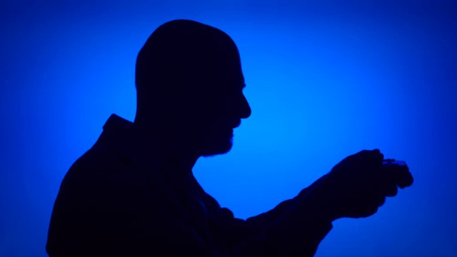 Silhouette of senior man gamer playing video game online. Male 's face in profile with game console on blue background. Black contour shadow of grandfather's half-face winning computer game