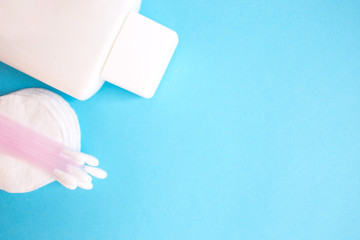 top view personal care products. white bottle, razor, ear sticks, cotton pads, toothbrush on blue background. copy space