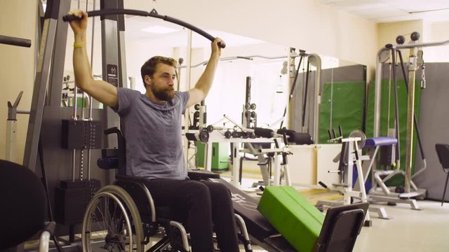 Young disabled man in wheelchair doing strength exercises for hands at the rehabilitation clinic