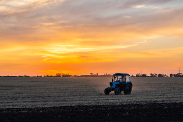 Fototapeta premium Agricultural machinery in the foreground carrying out work in the field on golden sunset