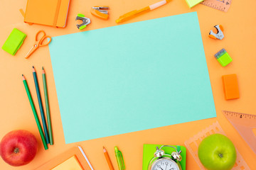 Back to school styled scene with orange and green school supplies on orange background, copy space on empty blue paper sheet © neirfy