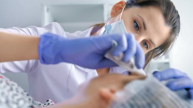Portrait female cosmetologist in mask uniform finishing procedure of permanent makeup