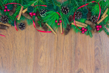A border of greenery with pine cones, red berry clusters,  red ribbon, and cinnamon sticks - obrazy, fototapety, plakaty