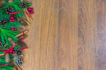 A border of greenery with pine cones, red berry clusters,  red ribbon, and cinnamon sticks