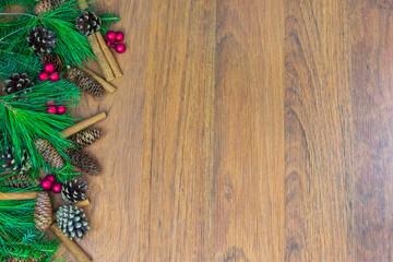 A border of greenery with pine cones, red berry clusters,  and cinnamon sticks