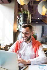 Fototapeta premium Portrait of smiling young entrepreneur using laptop while working in cafe, copy space