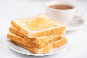 Fototapeta na wymiar Sliced bread with honey topping and cup of coffee on white table, delicious breakfast