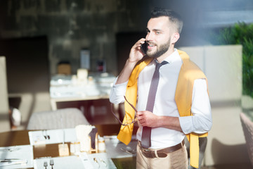 Waist up portrait of handsome businessman speaking by phone standing behind glass wall in cafe, copy space