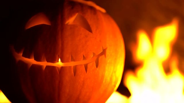 Smiling carved halloween pumpkin against of fiery explosion background. Glowing face trick or treat. Symbol of All Hallows' Eve or All Saints' Eve. 4k