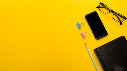 Mock up smartphone and office accessories on yellow background with copy space.view from above