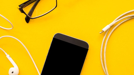 Smartphone and glasses with earphone on yellow background.Close up