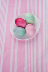 four multicolored painted Easter eggs on a white plate and  striped pink-white tablecloth. holiday easter greeting card, poster, wallpaper