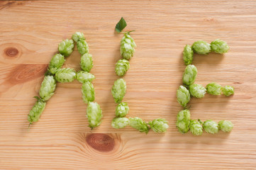 The inscription ale with hop cones on wooden background. Ingredient in beer industry. Craft beer brewing. For ale or lager