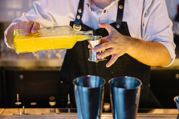 Expert barman is making cocktail with yellow juice at night club.