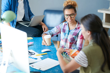 Portrait of contemporary African-American woman discussing creative  project with colleagues sitting at desk in modern office, copy space