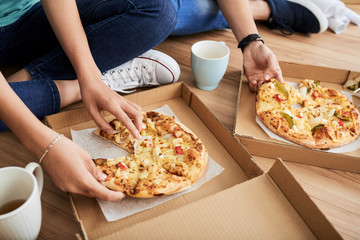 Young people sitting on room floor and eating delicious pizza