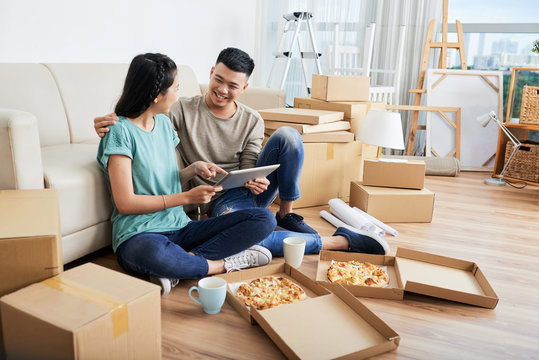 Happy Young Couple Eating Pizza And Discussing Interior Ideas After Moving In