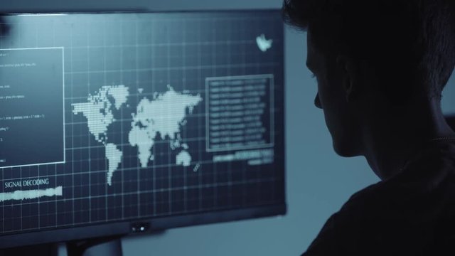 Young Hacker doing Attack on Data Servers and bank's account to still the secret credit card numbers. Working in sci-fi Dark Hideout in front of big screen with fantastic UI interface. Web tehcnology