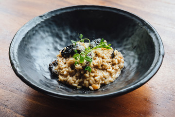 Risotto with mushroom, fresh herb and parmesan cheese in black plate on wooden table.