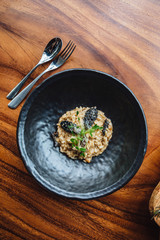 Risotto with mushroom, fresh herb and parmesan cheese in black plate on wooden table.