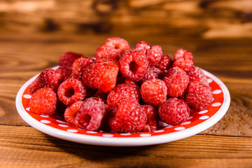 Ceramic plate with ripe raspberries on wooden table