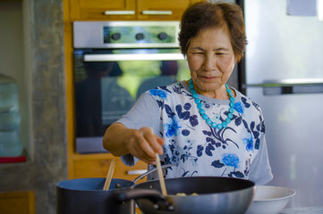 lifestyle portrait of senior happy and sweet Asian Japanese retired, woman cooking at home kitchen alone neat and tidy enjoying preparing meal