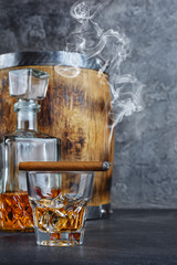 Strong alcoholic drink scotch whisky with ice cubes in old fashion glass and crystal decanter with smoking cigar