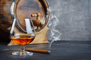 Strong alcoholic drink cognac in sniffer glass with smoking cigar and vintage wooden barrel in...
