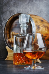 Strong alcoholic drink cognac in sniffer glass with crystal decanter and vintage wooden barrel in cellar