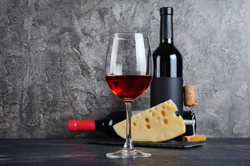 Red wine bottles with glass and cheese for tasting in cellar