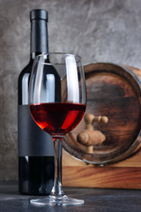 Red wine bottle with glass for tasting and wooden barrel in dark cellar